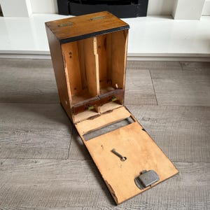 May include: A vintage wooden box with a hinged lid and a drop-down front panel. The box is divided into compartments and features a small key and a metal latch. The wood has a natural finish with dark trim.