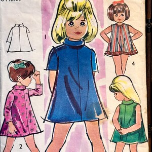 May include: Vintage sewing pattern featuring illustrations of girls' dresses. The designs include a blue dress, a pink dress with a polka dot pattern, a striped dress, and a green dress. The pattern also includes a line drawing of a collared shirt.