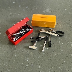 May include: A miniature tool set featuring a red toolbox, a yellow toolbox, and various tools. The tools include pliers, screwdrivers, a wrench, and a hammer. The tools are silver and black.