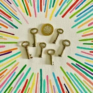 May include: A collection of seven vintage skeleton keys and a coin arranged on a white canvas. The keys are positioned around the coin, set against a backdrop of radiating, colourful lines, creating a striking and artistic arrangement.