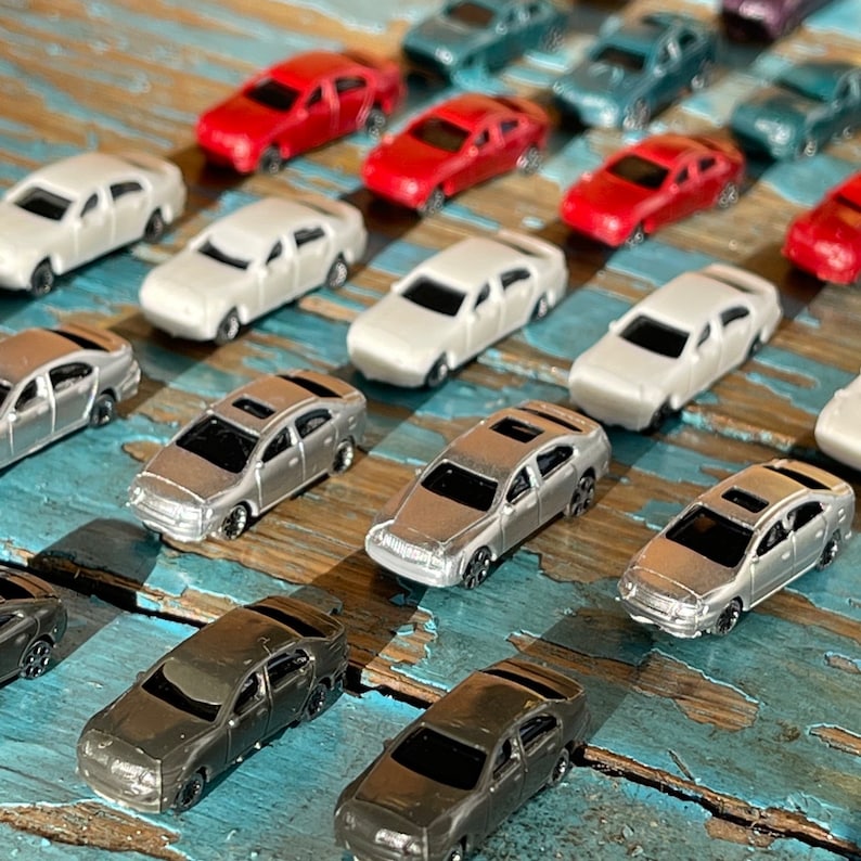 May include: A collection of miniature toy cars in various colors, including silver, white, red, and black. The cars are arranged in rows on a wooden surface.