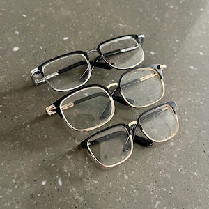 May include: Three pairs of spectacles with black frames and clear lenses. The top pair has silver accents, the middle pair has gold accents, and the bottom pair has gold accents.