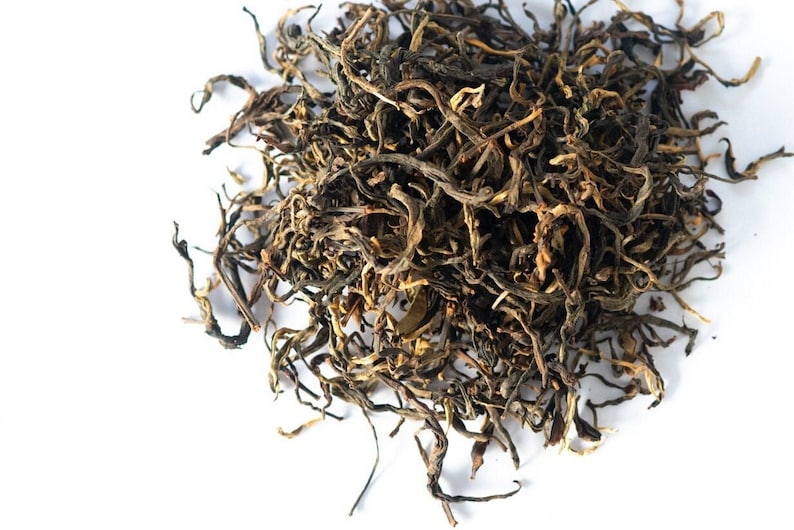 May include: Loose leaf black tea with long, thin, twisted leaves. The tea is a dark brown color with some lighter brown and green hues.