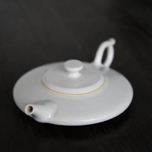 May include: A white ceramic teapot with a lid and a spout. The teapot has a simple design and is perfect for brewing tea.