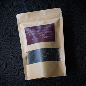 May include: A brown paper bag with a clear window showing loose leaf black tea inside. The bag has a label that reads "Ancient Trees Black Tea" with a description of the tea.