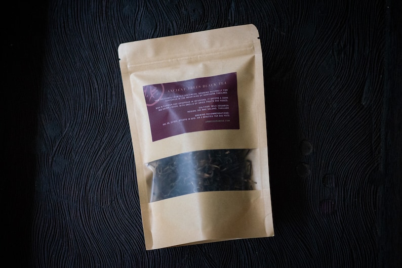 May include: A brown paper bag with a clear window showing loose leaf black tea inside. The bag has a label that reads "Ancient Trees Black Tea" with a description of the tea.