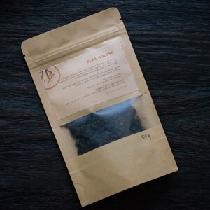 May include: A brown paper pouch with a clear window showing loose black tea leaves. The pouch has a label with the text "Ruby Oolong" and a description of the tea.