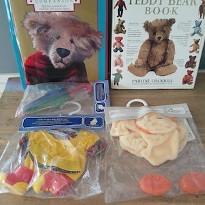 May include: A collection of teddy bear-themed items. Includes two books, one titled "Teddy Bear Book" and the other "Being a Book of Their Life and Times." Also, a yellow raincoat set with red boots, a beige outfit, and an umbrella.