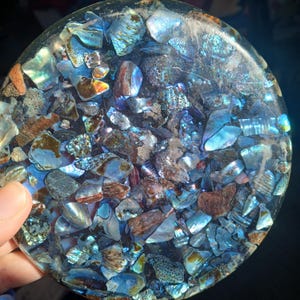 May include: A round, blue and iridescent resin coaster with embedded pieces of abalone shell.