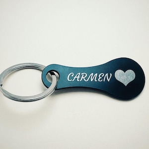 Può includere: Un portachiavi nero con un portachiavi argentato. Il portachiavi presenta il nome "Carmen" in corsivo bianco e un simbolo a cuore bianco. Un accessorio personalizzato.