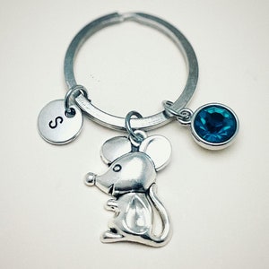 Può includere: Portachiavi d'argento con un piccolo ciondolo a forma di topo, un ciondolo di cristallo blu e un ciondolo d'argento con la lettera "S" su di esso.
