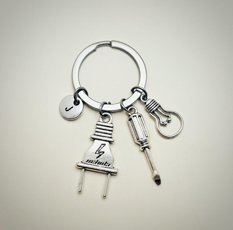 May include: Silver keychain with a lightbulb, screwdriver, and electrical plug charm. The plug charm has a lightning bolt and the letter 'J' is on a round charm.