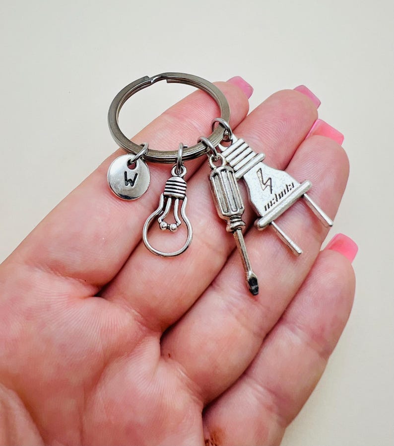 May include: Silver keychain with a lightbulb, screwdriver, and electrical plug charm. The keychain also has a small charm with the letter "W" on it.