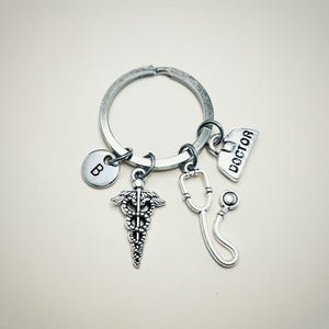 May include: Silver keychain with a medical symbol charm, a stethoscope charm, a charm that says "DOCTOR", and a charm with the letter "B".