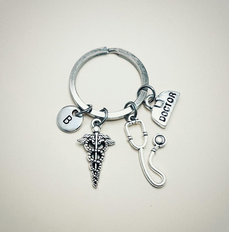 May include: Silver keychain with a medical symbol charm, a stethoscope charm, a charm that says "DOCTOR", and a charm with the letter "B".