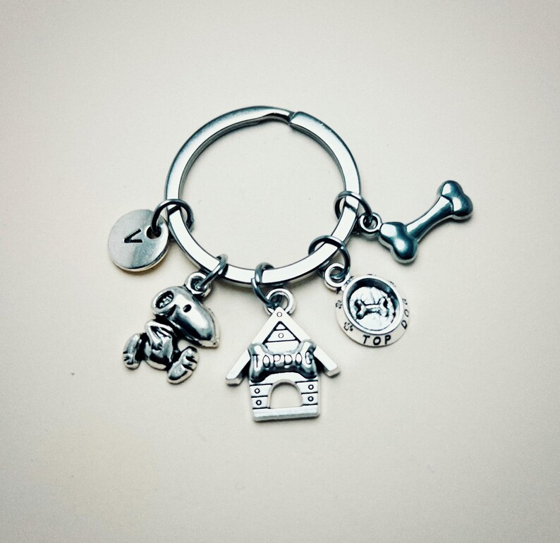 May include: Silver keychain with a dog bone, dog house, dog bowl, and a letter A charm. The dog house charm says "Top Dog".