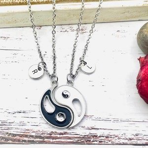 Può includere: Due collane d'argento con un ciondolo yin yang e ciondoli con iniziali. I ciondoli sono incisi con le lettere "R" e "L".