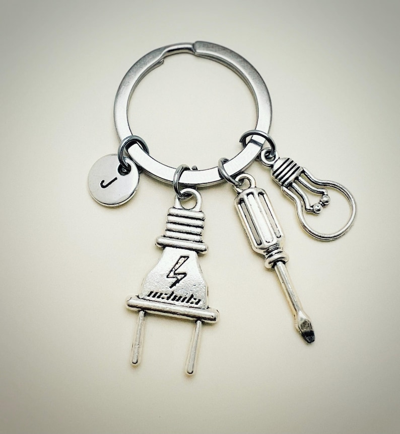 May include: Silver keychain with a lightbulb, screwdriver, and electrical plug charm. The plug charm has a lightning bolt design. The keychain also has a silver initial charm with the letter "J" on it.