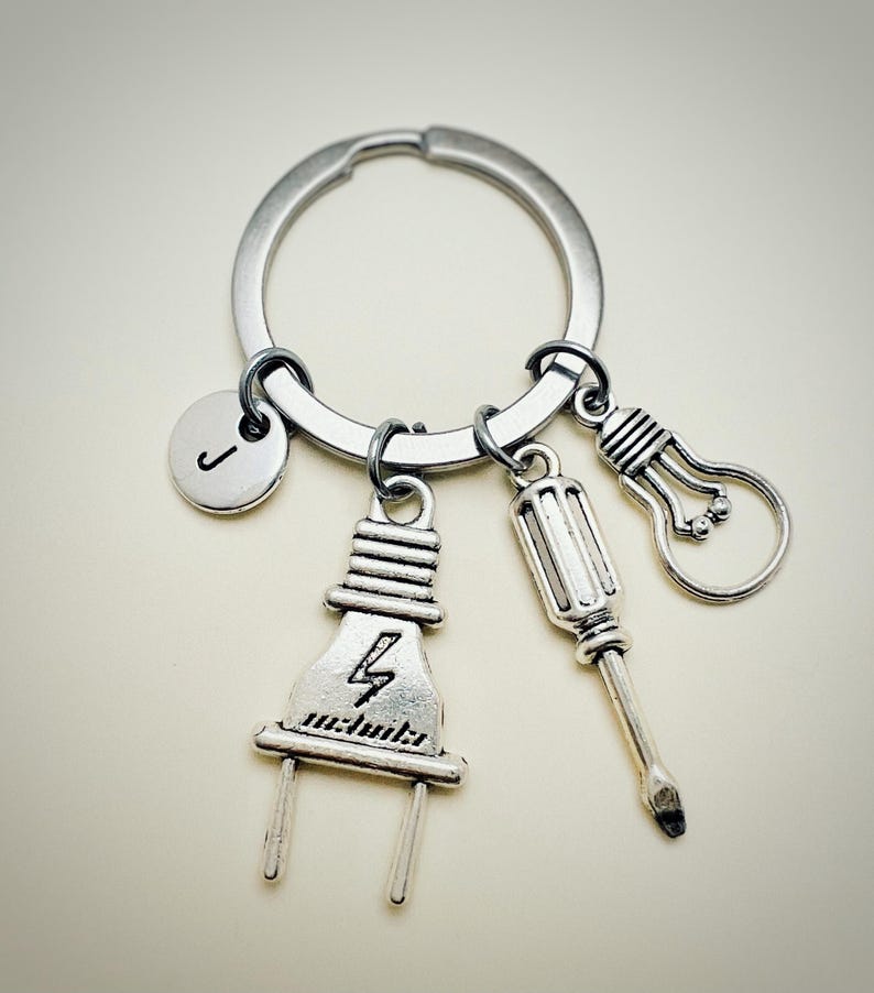 May include: Silver keychain with a lightbulb, screwdriver, and electrical plug charm. The keychain also has a silver charm with the letter J.