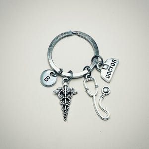 May include: Silver keychain with a medical symbol charm, a stethoscope charm, a charm with the word "DOCTOR" on it, and a charm with the letter "B" on it.