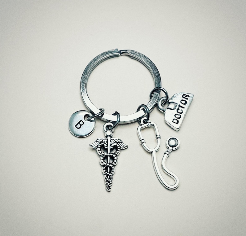 May include: Silver keychain with a medical symbol charm, a stethoscope charm, a charm with the word "DOCTOR" on it, and a charm with the letter "B" on it.