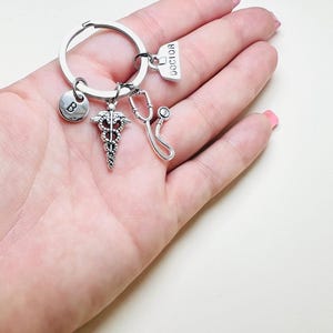 May include: Silver keychain with a medical symbol charm, a stethoscope charm, a charm with the word "DOCTOR" on it, and a charm with the letter "B" on it.