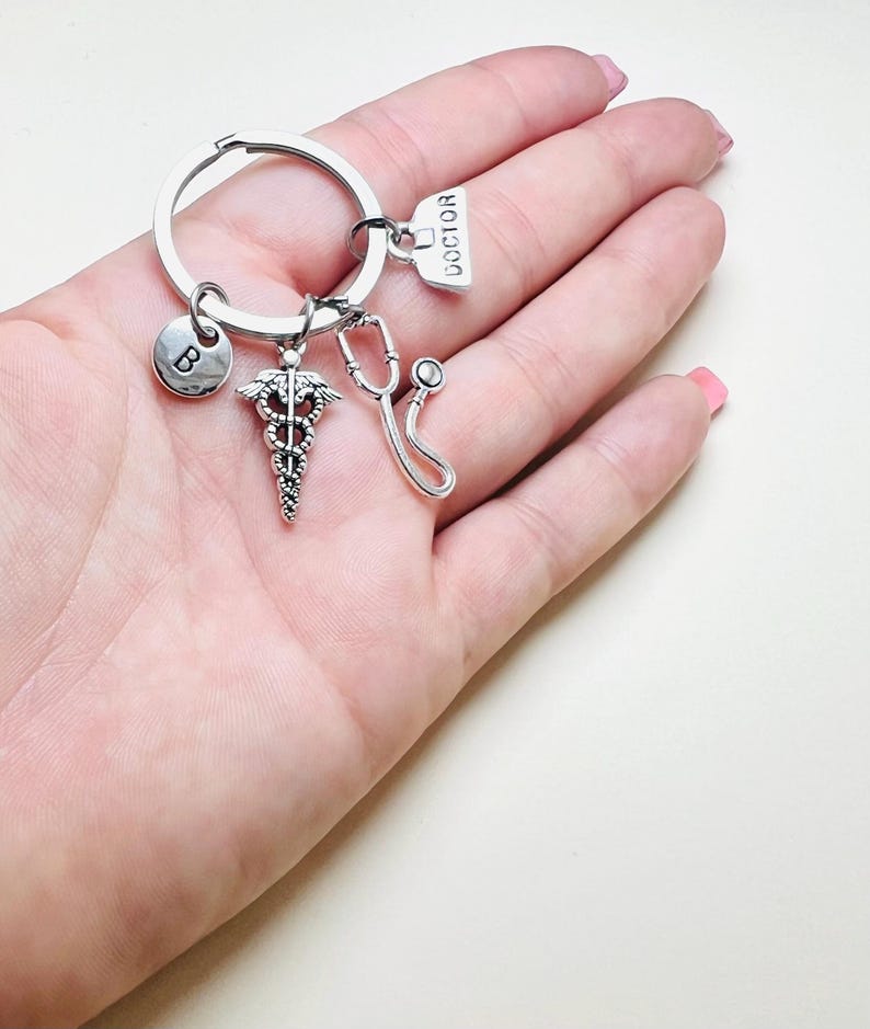May include: Silver keychain with a medical symbol charm, a stethoscope charm, a charm with the word "DOCTOR" on it, and a charm with the letter "B" on it.