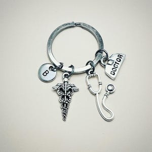 May include: Silver keychain with a medical symbol charm, a stethoscope charm, a charm that says "DOCTOR", and a charm with the letter "B".