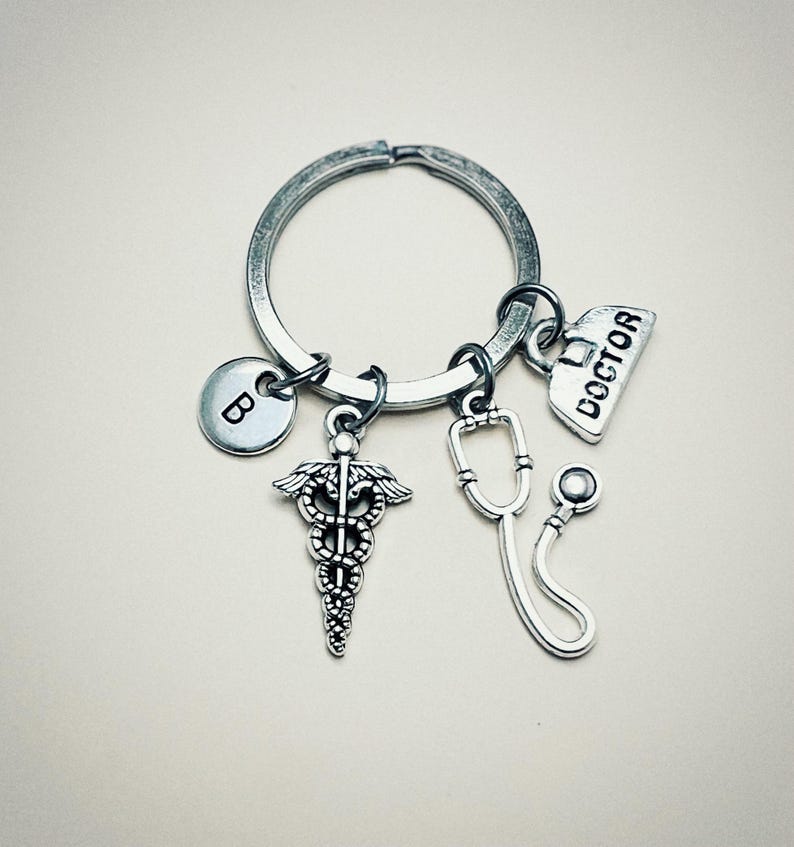 May include: Silver keychain with a medical symbol charm, a stethoscope charm, a charm that says "DOCTOR", and a charm with the letter "B".