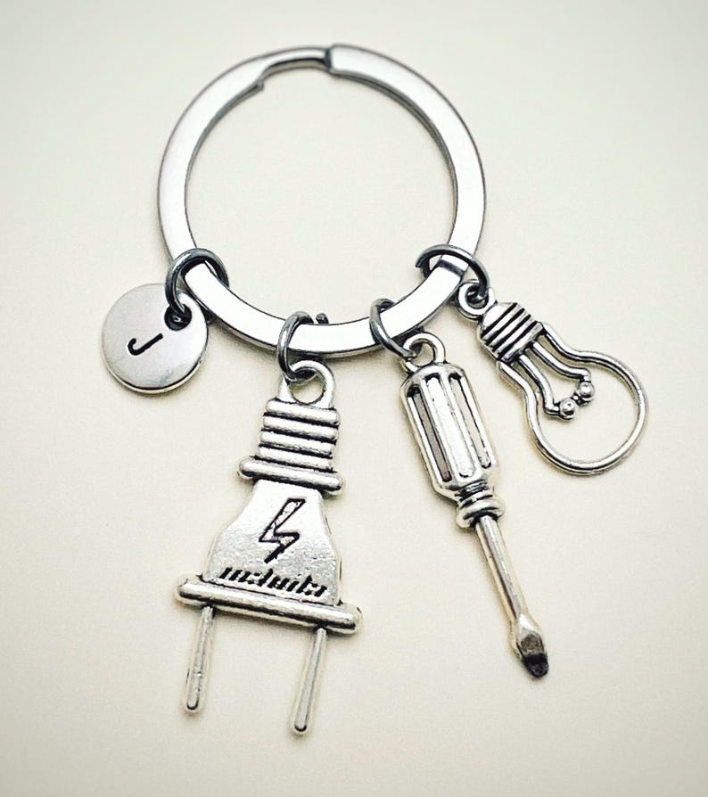May include: Silver keychain with a lightbulb, screwdriver, and electrical plug charm. The keychain also has a silver charm with the letter J.