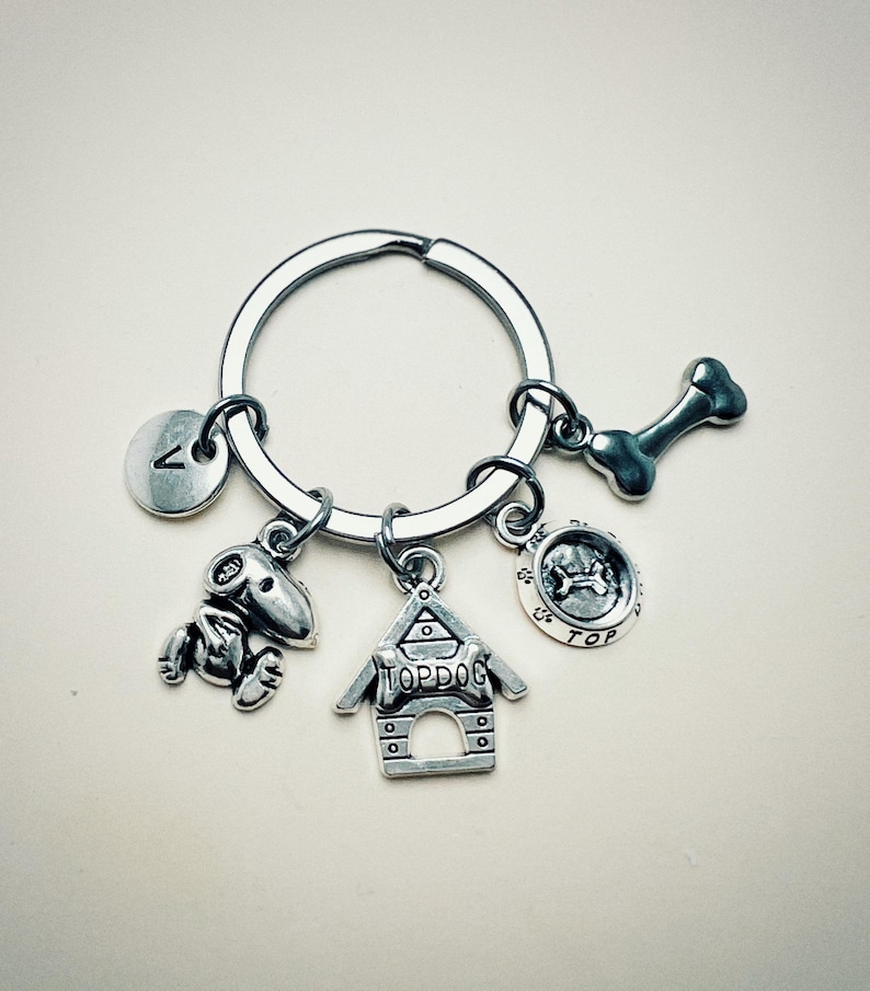 May include: Silver keychain with a dog bone charm, a dog house charm with the text "Top Dog", a dog paw print charm with the text "Top", and a letter "A" charm.