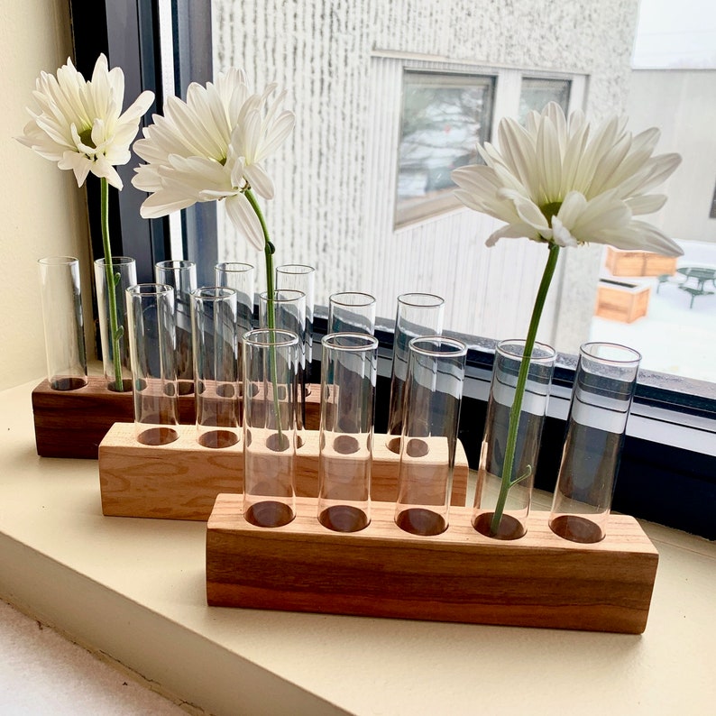 May include: A set of clear glass test tubes with white flowers in them. The test tubes are arranged in a wooden stand with a natural wood grain finish.