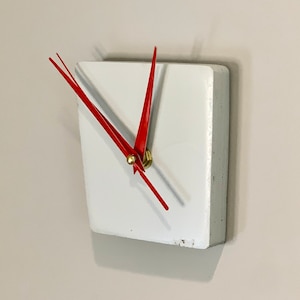 May include: A white square clock with red hands. The clock is mounted on a white wall.