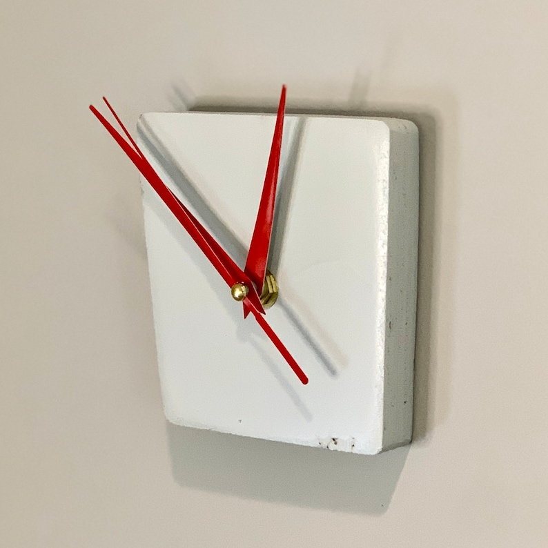 May include: A white square clock with red hands. The clock is mounted on a white wall.