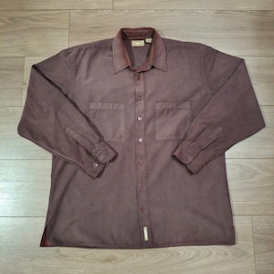 May include: A long-sleeved, button-down shirt in a muted burgundy color. The shirt features two chest pockets, a collared neckline with a darker brown velvet-like material, and buttoned cuffs. The shirt is made of a soft, textured fabric.