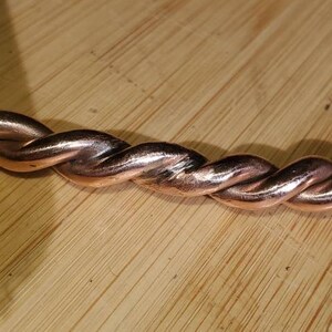 May include: A close-up of a copper bracelet with a twisted design. The bracelet is made of a single piece of copper wire that has been twisted together to create a rope-like effect.