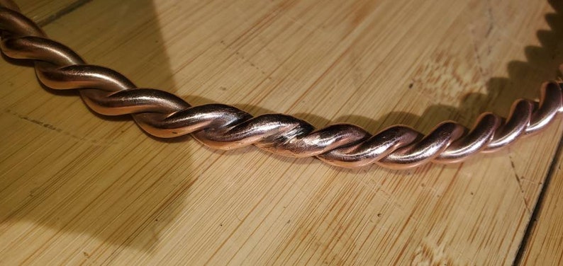 May include: A close-up of a copper bracelet with a twisted design. The bracelet is made of a single piece of copper wire that has been twisted together to create a rope-like effect.