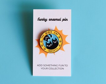 May include: A yellow and blue enamel pin with a black cat design. The pin says "The Black Cat Society" in a circle with stars around it. The pin is on a white card that says "funky enamel pin" and "Add something fun to your collection".