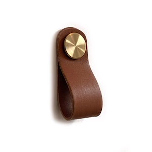 Könnte beinhalten: Ein brauner Leder-Schrankgriff mit einem Messingknopf.