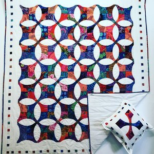 May include: A colorful quilt with a repeating pattern of interlocking circles in shades of red, blue, purple, and green. The quilt has a white border with small square accents. A matching pillow is also present.