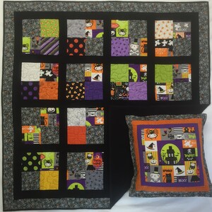 Puede incluir: Un juego de edredón y cojín con temática de Halloween. El edredón presenta un diseño de patchwork con varios patrones de Halloween en naranja, morado, verde y negro. El cojín tiene un diseño a juego con una casa embrujada y personajes espeluznantes.