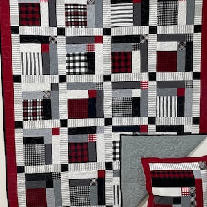 May include: A patchwork quilt and pillow set featuring a mix of black, white, gray, and red fabrics. The quilt has a red border and a geometric pattern with squares and rectangles. The pillow mirrors the quilt's design.