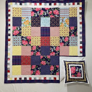 May include: A patchwork quilt and pillow set featuring a variety of floral and geometric patterns in shades of red, blue, yellow, and white. The quilt has a navy blue border with a plaid design. The pillow has a matching floral pattern.