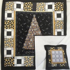 以下が含まれることがあります： クリスマスをテーマにしたキルトと枕のセット。キルトは、黒い背景に装飾されたクリスマスツリーの画像が中心にあり、黒、金、白の模様の正方形で囲まれています。枕も同様のデザインです。