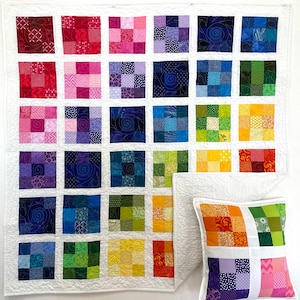 May include: A colorful patchwork quilt and pillow set. The quilt features a grid of squares in a rainbow of colors, from red to purple to green and yellow. The pillow mirrors the quilt's design, with a white border.