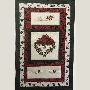 May include: A Christmas-themed quilt featuring a central poinsettia wreath and rectangular panels with the phrases "Merry Christmas" and "Joy, Peace." The quilt has a white background with red poinsettia and holly leaf patterns, framed by black and white striped borders.