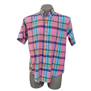 Puede incluir: Una camisa de manga corta con botones y estampado de cuadros rosa, azul y verde.