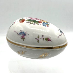 May include: A white porcelain egg-shaped trinket box with a gold trim and floral designs in shades of pink, blue, yellow, and green.