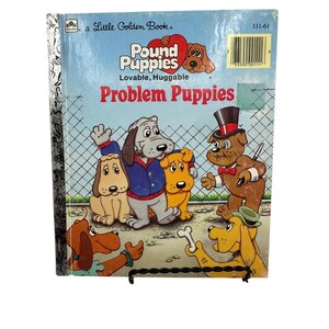 May include: A Little Golden Book titled "Pound Puppies: Problem Puppies". The cover features a group of cartoon puppies, including a grey puppy wearing a blue jacket, a yellow puppy, a brown puppy wearing a top hat and bow tie, and a brown puppy wearing a green hat. The book is part of the "Pound Puppies" series, which features lovable and huggable puppies.