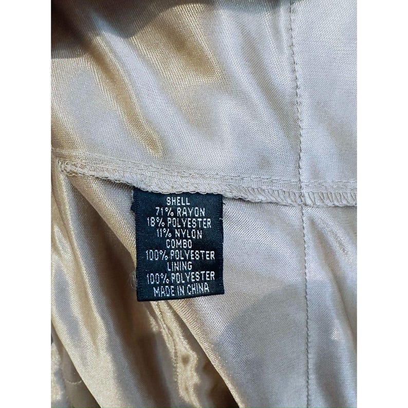 Może przedstawiać: Zbliżenie metki z informacjami o składzie materiału. Na metce widnieje napis "SHELL 71% RAYON 18% POLYESTER 11% NYLON COMBO 100% POLYESTER LINING 100% POLYESTER MADE IN CHINA". Etykieta jest czarna z białym tekstem.